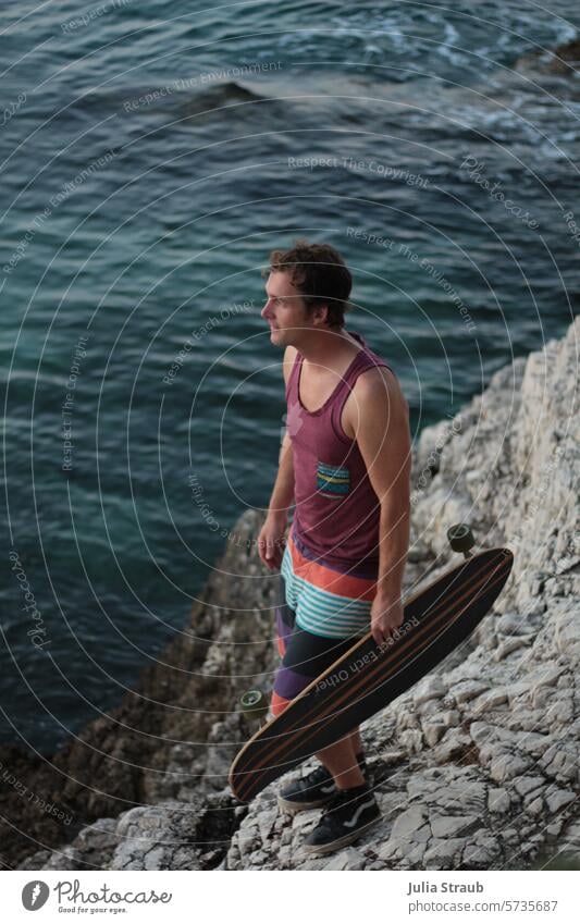 Kurze Pause mit Blick aufs Meer Küste Felsen Mann Skateboarder Longboard Sommer Wasser Erholung Urlaub Auszeit Lässigkeit Cool klares Meer schöner Mann