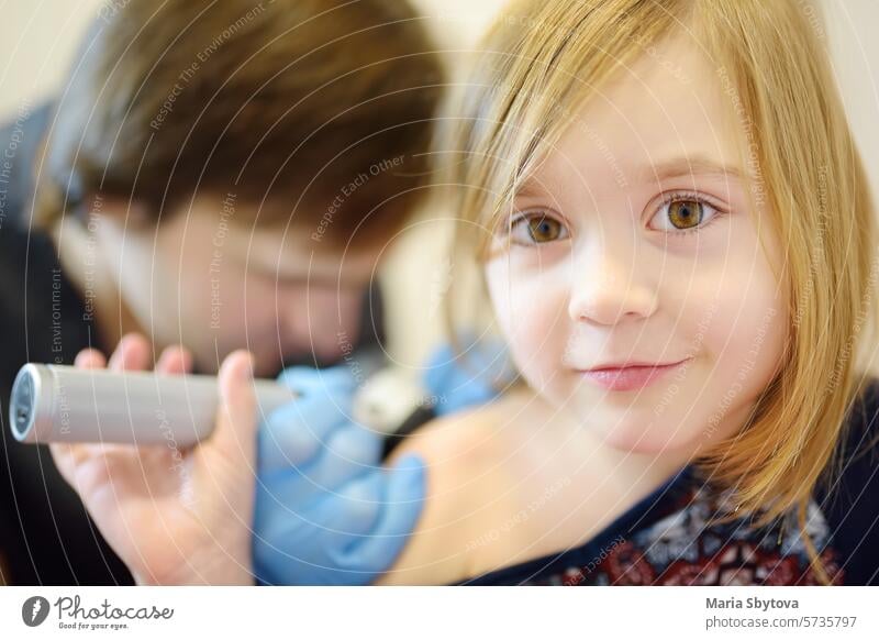 Ein fürsorglicher Arzt untersucht Muttermale auf der Haut eines kleinen Kindes. Ein Dermatologe betrachtet einen Ausschlag auf dem Rücken eines Mädchens mit einem Dermatoskop.