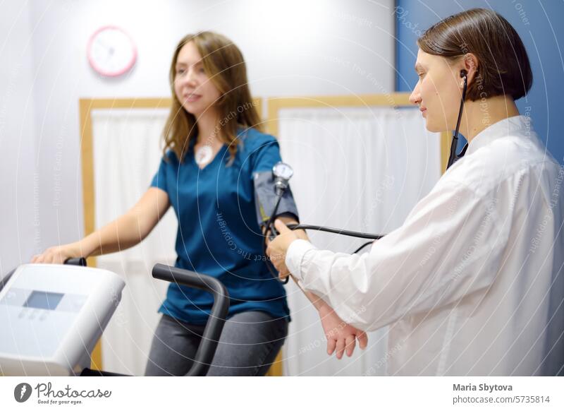 Weiblicher Arzt Kardiologe misst Druck mit Patienten während Fahrrad Übung für die Untersuchung Herz-Kreislauf-System im medizinischen Büro der Klinik. Junge Frau Training auf Fahrrad-Simulator.