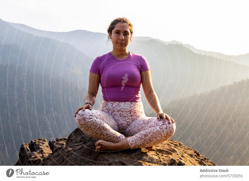 Eine Frau in Yogastellung sitzt ruhig auf einem Berg, während die untergehende Sonne ein warmes Licht auf die bewaldete Landschaft wirft Meditation Pose