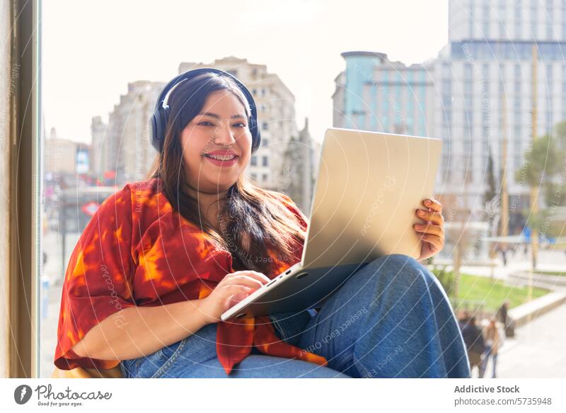 Lächelnde Frau mit Laptop und Kopfhörern in städtischer Umgebung Großstadt Musik heiter urban Umwelt sonnig Gebäude Technik & Technologie online Freizeit lässig