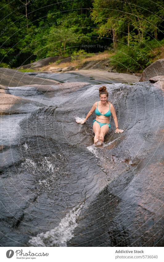 Eine Frau gleitet voller Freude eine glatte, natürliche Felsenrutsche in den grünen Wäldern von Langkawi hinunter und genießt den Spaß an der Natur Sliden Fluss