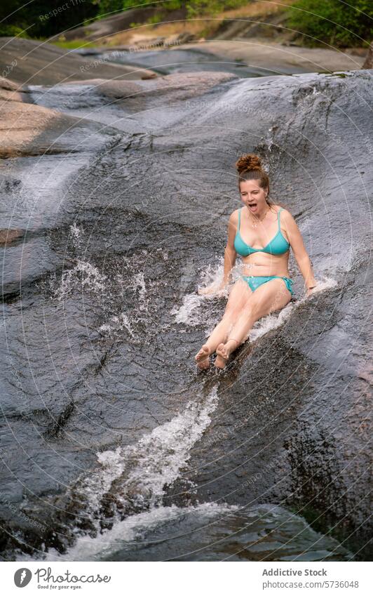Eine Frau gleitet voller Freude eine glatte, natürliche Felsenrutsche in den grünen Wäldern von Langkawi hinunter und genießt den Spaß an der Natur Sliden Fluss