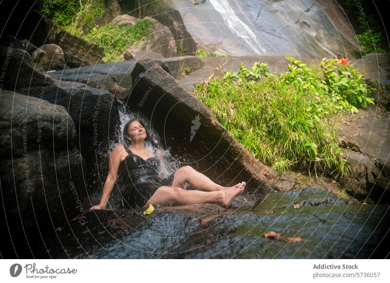 Eine Frau lehnt sich auf einem Felsen zurück und spürt das sanfte Rauschen eines Wasserfalls in der üppigen Umgebung von Langkawi, Malaysia ruhig fließen