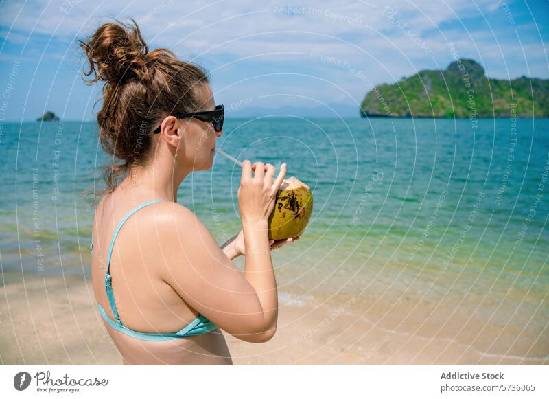 Eine Frau genießt ein frisches Kokosnussgetränk an einem sonnigen Strand mit dem malerischen Langkawi-Archipel im Hintergrund trinken Inselgruppe Erfrischung