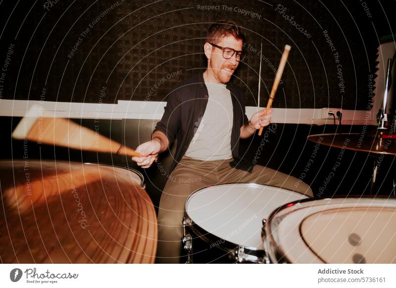 Dynamischer männlicher Schlagzeuger, der in einem schwach beleuchteten Raum spielt Mann Trommel Musik Band Instrument Spielen Brille Lächeln energetisch