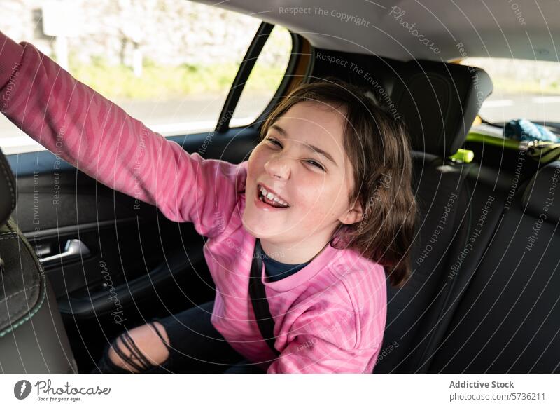 Ein glückliches Kind genießt eine Autofahrt Mädchen Glück Freude Aufregung Lächeln winkend Sitz Fahrzeug Innenbereich Reise reisen Fröhlichkeit Freizeitkleidung
