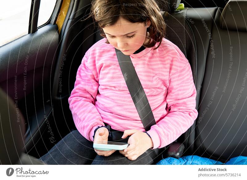Kind benutzt Smartphone im Autositz Sicherheit Sicherheitsgurt Fahrzeug Technik & Technologie Handy reisen Youngster Autoreise rosa Pullover vertieft Spielen
