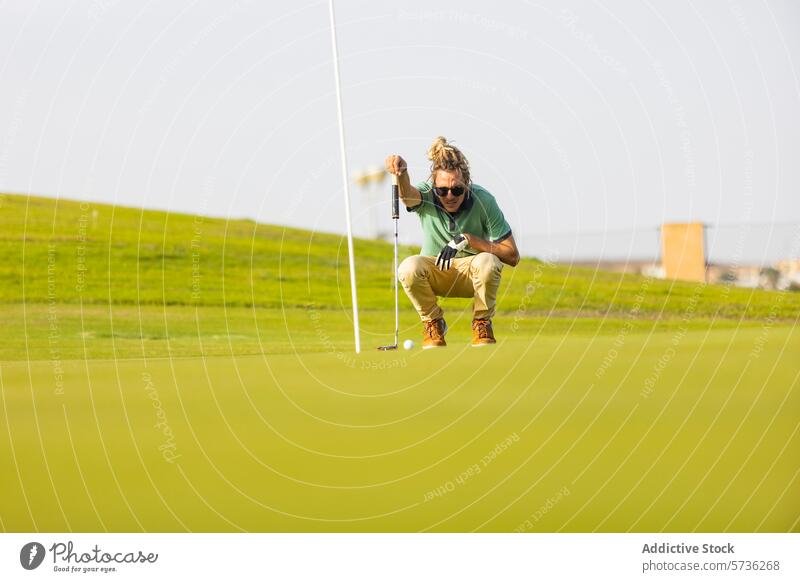 Einzigartiger Golfer mit Dreadlocks zielt auf das Grün Kurs grün hocken Putten Sonnenlicht blond Rastalocken unkonventionell Sport Zeitgenosse Ziel Athlet