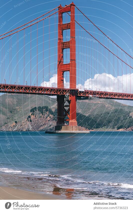 Ein atemberaubender Blick auf die Golden Gate Bridge vom Sandstrand aus gesehen, mit sanften Wellen, die an den Strand plätschern, und Hügeln in der Ferne