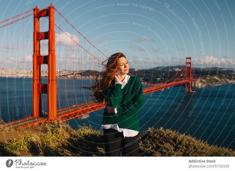 Eine junge Frau genießt die Wärme der Frühlingssonne mit der berühmten Golden Gate Bridge und der Skyline von San Francisco in der Ferne Sonne kultig