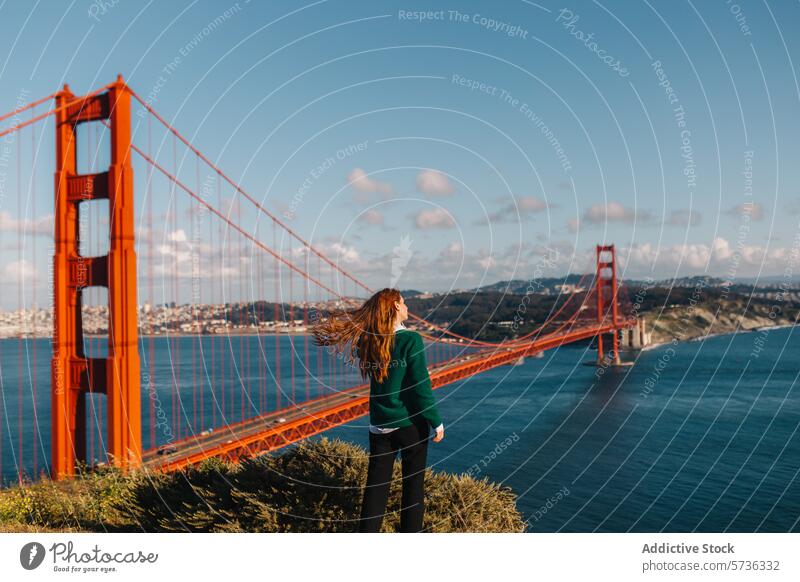 Rückenansicht Frau steht in Ehrfurcht, als der Wind ihr Haar erfasst, mit Blick auf die herrliche Golden Gate Bridge an einem strahlenden Frühlingstag
