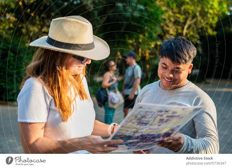 Junge Reisende konsultieren eine Landkarte in einem sonnigen Park Reisender Beratung junger Erwachsener Gespräch im Freien Baum Mitreisender verbindlich