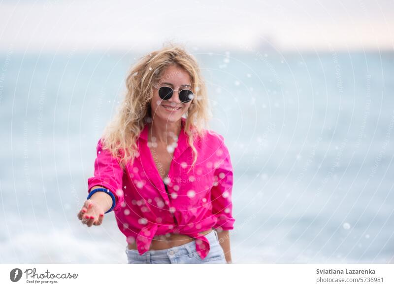 Eine schöne Frau mit Sonnenbrille und rosa Hemd bespritzt das Meerwasser. im Freien Sommer eine Person Kaukasier Spaß Natur Lächeln Frauen heiter Lifestyle