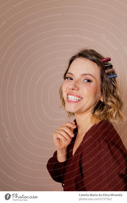 Junge Frau lächelnd, mit braunem Haar und brauner Bluse auf isoliertem beigem Hintergrund. Mit Haar-Accessoires. 20-25s erstaunt schön Schönheitssalon