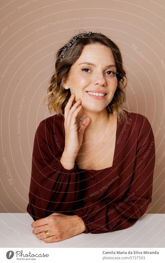 Junge Frau lächelnd, mit braunem Haar und brauner Bluse auf isoliertem beigem Hintergrund. Mit Haar-Accessoires. 30-35s erstaunt schön Schönheitssalon