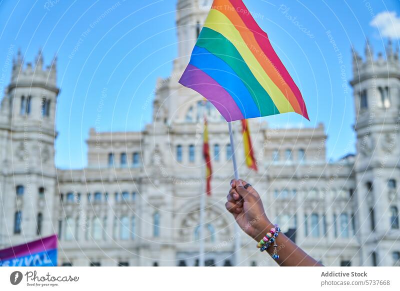 Eine Hand schwenkt die Regenbogenfahne bei einer LGBTIQ-Pride-Veranstaltung Stolz Regenbogenflagge Arme Solidarität historisches Gebäude Hintergrund Feier