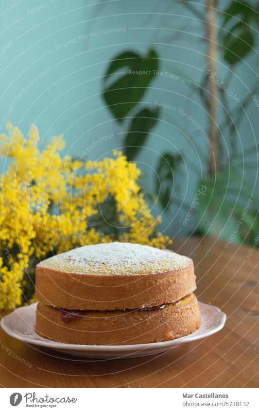 Mit Marmelade gefüllte Maria-Luisa-Torte auf einem Holztisch mit einem Hintergrund aus gelben Blumen. Pasteten Gebäck Dessert Lebensmittel Kuchen selbstgemacht