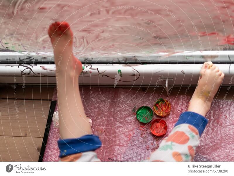 Ein Kind malt mit seinen Füßen an ein Fenster Kinderkunst Leben mit Kindern rot gelb bunt Hand Finger Freude Spaß Fenstermalerei Kreativ mit Kindern
