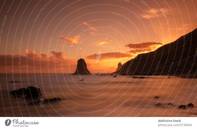 Ein feuriger Sonnenuntergang wirft ein warmes Licht auf die mystischen Felsen und das ruhige Wasser der Playa de Benijo, Teneriffa glühen Seeschornstein Himmel