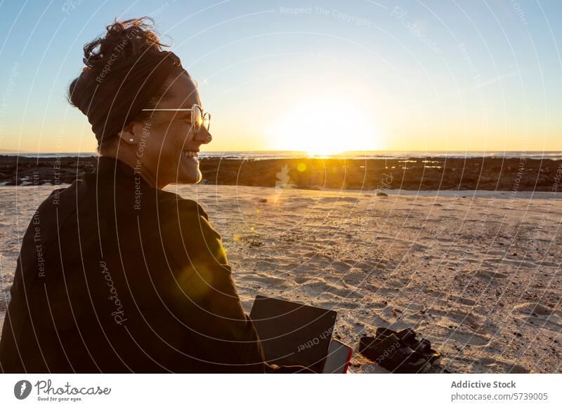 Lächelnder digitaler Nomade bei der Arbeit am Strand bei Sonnenuntergang Frau Laptop reisen Lifestyle im Freien abgelegen Job Technik & Technologie Drahtlos