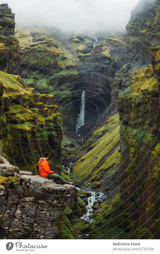 Anonymer Wanderer mit Blick auf einen majestätischen Wasserfall in Island Abenteuer reisen Natur Landschaft Felsen Saum Klippe grün Moos im Freien Erkundung