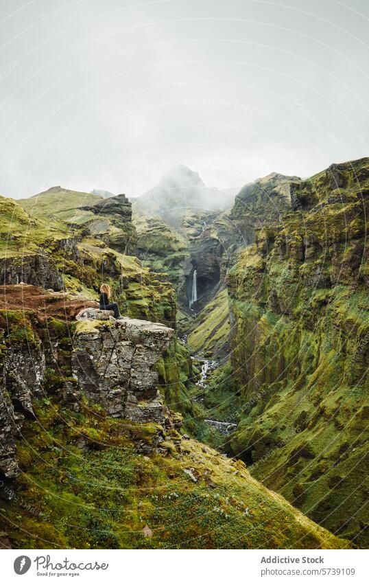 Anonyme Frau sitzt auf einer Klippe und betrachtet die Natur an einem abgelegenen isländischen Wasserfall Island Abenteuer Einsamkeit Grün Landschaft Reisender