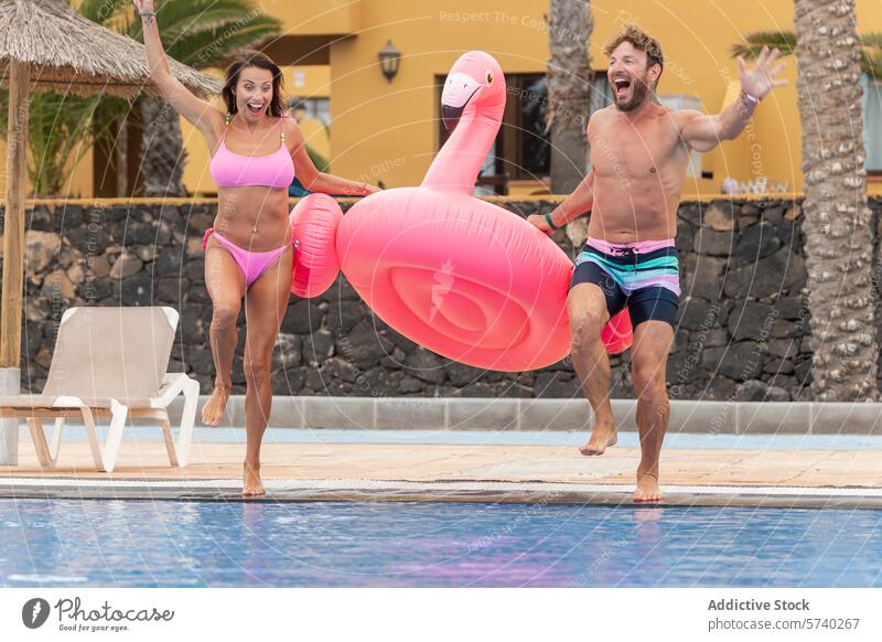 Fröhliches Paar spielt mit aufblasbarem Flamingo am Pool spielerisch Freude Badebekleidung Urlaub Freizeit Spaß Sommer Feiertag Aufregung Fröhlichkeit im Freien