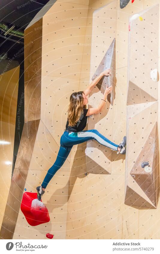 Frau erklimmt mit Entschlossenheit eine Indoor-Kletterwand im Innenbereich Klettern Wand Beweglichkeit Stärke Erreichen herausfordernd Halt meisterhaft Skala
