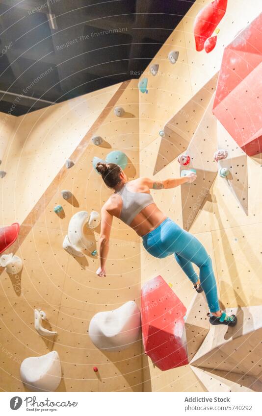 Kletterer beim Aufstieg an einer Boulderwand in einer Halle Aufsteiger im Innenbereich Bouldern Wand Frau Stärke Beweglichkeit aufsteigen gekonnt