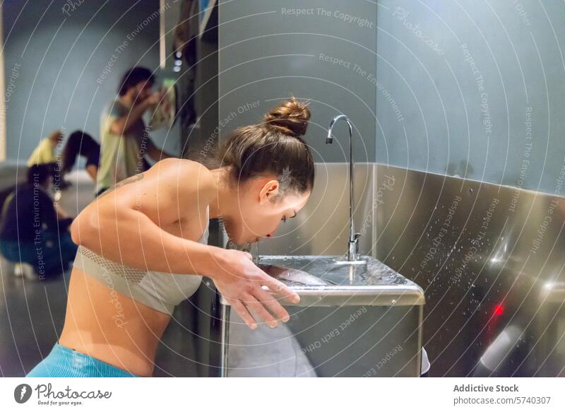 Frau erfrischt sich am Wasserbrunnen Wasserfontäne erfrischend Training trinken Fitness Fitnessstudio Hydratation Sportbekleidung Übung Gesundheit Lifestyle