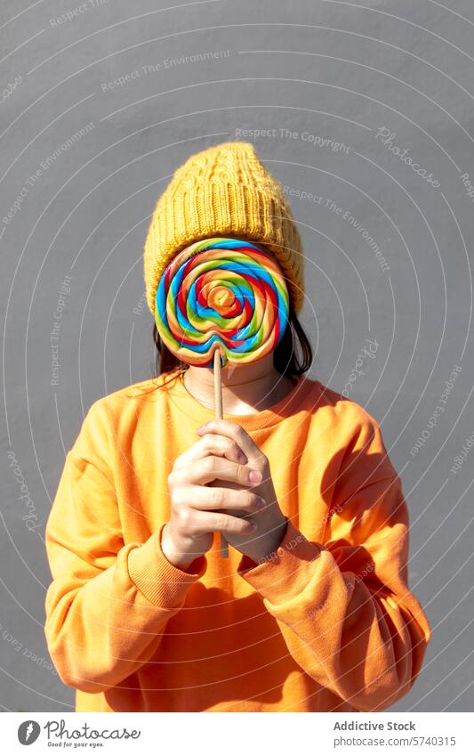 Person mit buntem Lutscher, der ihr Gesicht bedeckt Lollipop Bonbon farbenfroh süß Leckerbissen verstecktes Gesicht verdunkelt Verkleidung spielerisch