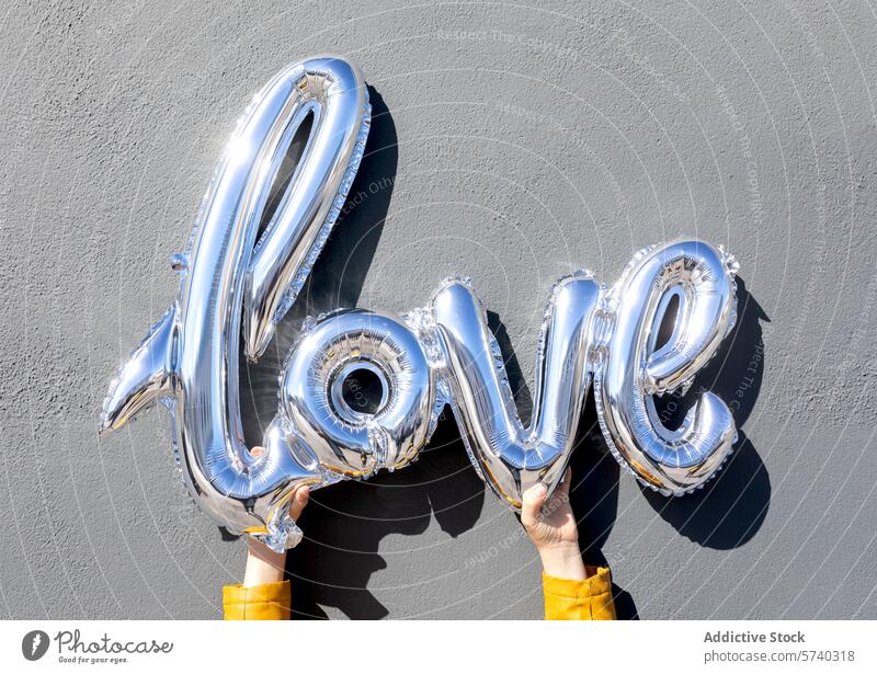 Silberne Ballonbuchstaben in der Hand, auf denen Liebe steht Luftballon Halt Brief Wort grauer Hintergrund Feier Dekoration & Verzierung Valentinsgruß Romantik