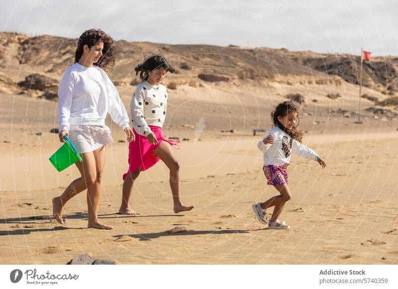 Eine liebevolle, alleinerziehende Mutter spaziert mit ihren beiden kleinen Töchtern am Strand entlang, wobei die Jüngste fröhlich vorausläuft Familie Kinder