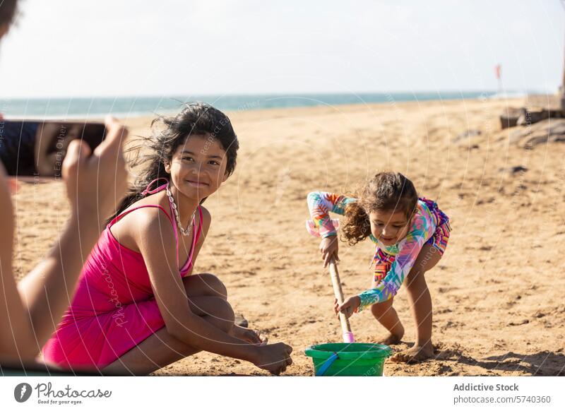 Anonyme alleinerziehende Mutter fängt einen kostbaren Moment ein, als ihre Töchter an einem sonnigen Strand mit Sand spielen, voller Freude und Lachen Spielzeit