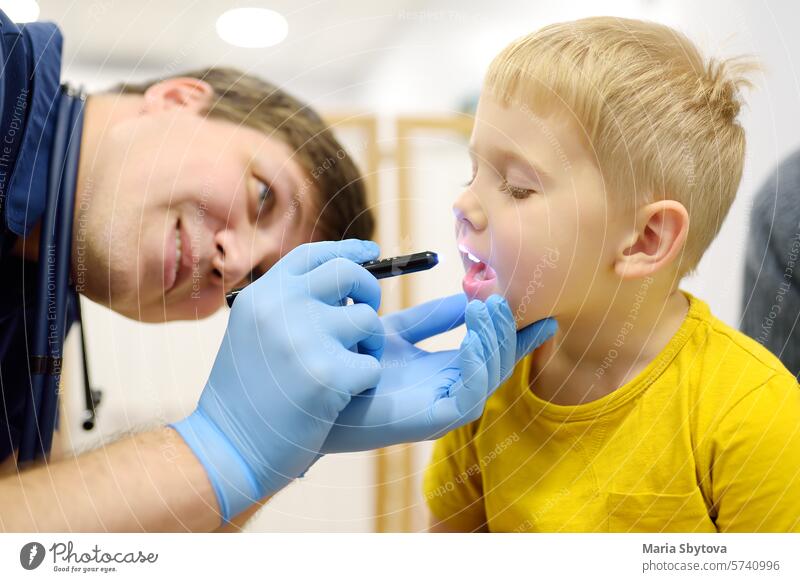 Ein niedlicher kleiner Junge und seine Mutter haben einen Termin bei einem Kinderarzt. Der Kinder-HNO-Arzt untersucht den Rachen eines kleinen Patienten mit einer Taschenlampe.