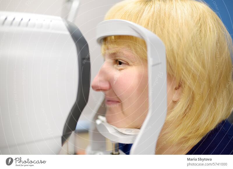 Porträt einer reifen Frau beim Besuch eines Augenarztes zur mikroskopischen Untersuchung von Augenlidern, Sklera, Bindehaut, Iris, Linse und Hornhaut. Untersuchung des Augenhintergrunds eines Patienten durch einen Augenarzt mit Netzhautscanner