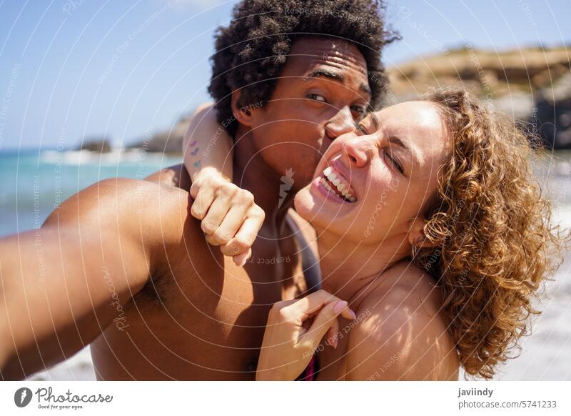 Schwarzer Mann küsst die Wange seiner glücklichen Freundin, während er ein Selfie macht Paar fotografieren Kuss Umarmung Feiertag Freude Sonnenlicht Strand