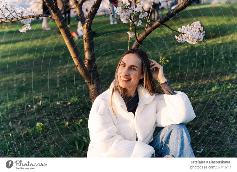 Frau genießt den Frühling im Gras sitzend im Stadtpark unter blühenden Bäumen jung Garten Natur Kirsche im Freien Blüte Überstrahlung Schönheit Park schön lang