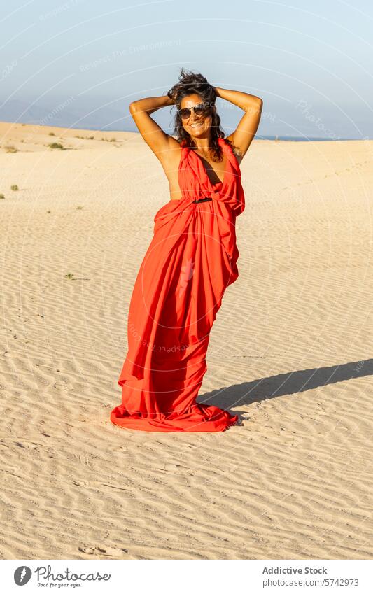 Frau in wallendem roten Kleid genießt die Sonne in der Wüste wüst Dunes Freude pulsierend stehen Hände hippe sandig übersichtlich Himmel Lächeln Sonnenbrille