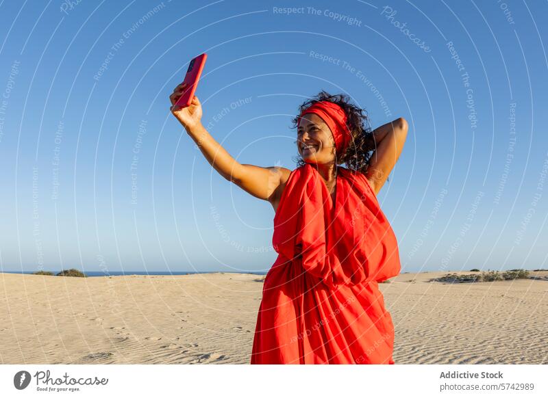 Fröhliche Frau nimmt Selfie in der Wüste mit Telefon rotes Kleid wüst Düne Handy Lächeln Freude Fröhlichkeit Blauer Himmel Apparatur Gerät Sommer im Freien