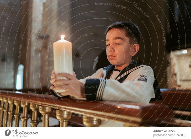 Ein nachdenklicher Junge hält eine brennende Kerze während seiner Erstkommunion in einer ruhigen Kirchenumgebung Gelassenheit Reflexion & Spiegelung beleuchtet