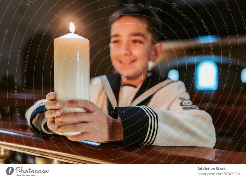 Ein lächelnder Junge in seiner Erstkommunionkleidung hält eine Kerze mit einer hellen Flamme, die Freude und Glauben an die Kirche symbolisiert freudig