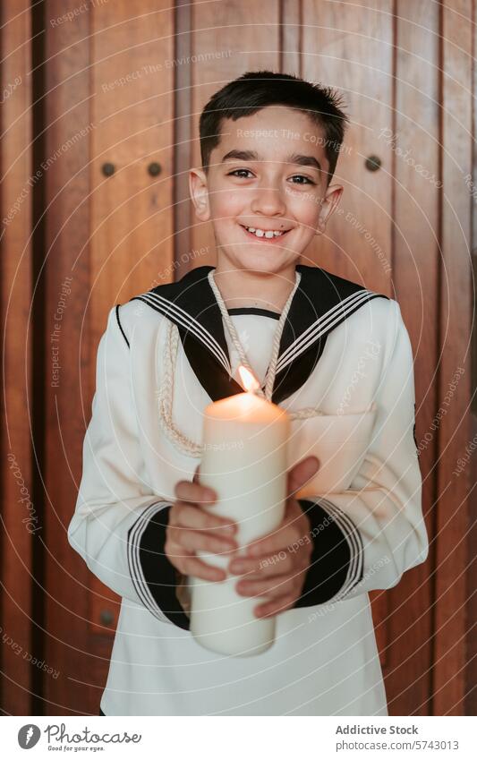 Ein kleiner Junge in seiner Erstkommunionkleidung hält mit einem warmen Lächeln eine brennende Kerze, die das Licht des Glaubens symbolisiert. Porträt Kommunion