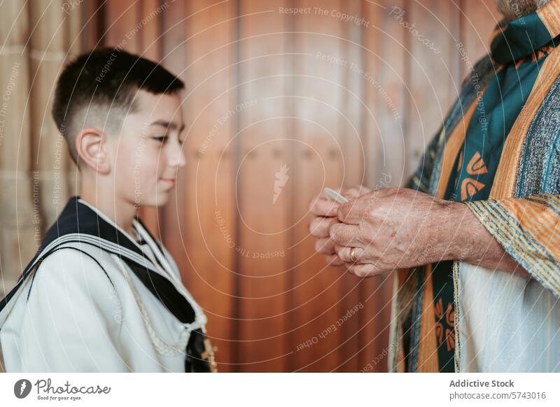 Ein Junge in Erstkommunionskleidung schaut zu, wie ein anonymer Priester sich darauf vorbereitet, den Segen zu erteilen - ein Moment des Glaubens und der Tradition