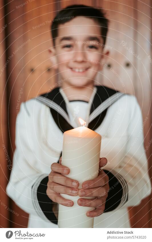 Ein zufriedener Junge im Erstkommunionkleid hält eine Kerze, deren Flamme das Licht Christi symbolisiert, mit sanftem Blick Lächeln Kleid Symbol Christus Fokus