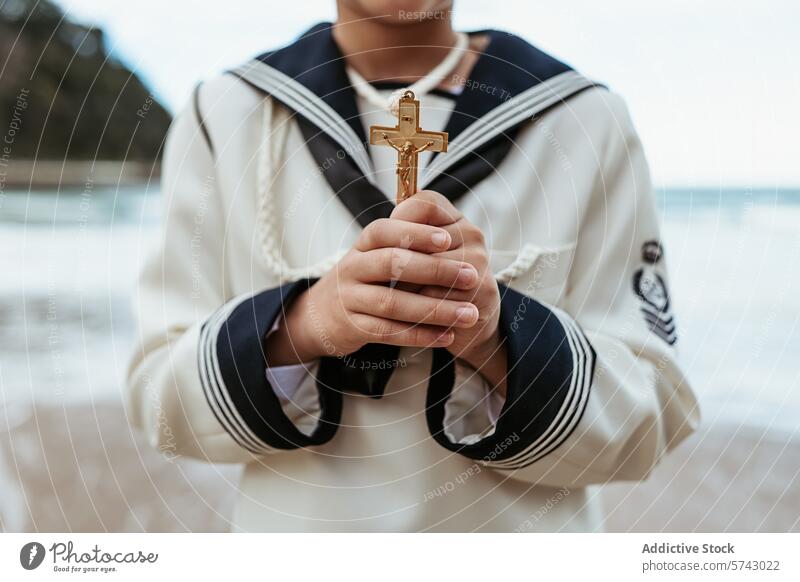 Fokussiertes Bild von anonymen Kinderhänden, die ehrfürchtig ein goldenes Kruzifix während einer Erstkommunionsfeier am Meer halten Nahaufnahme Hände Ehrfurcht