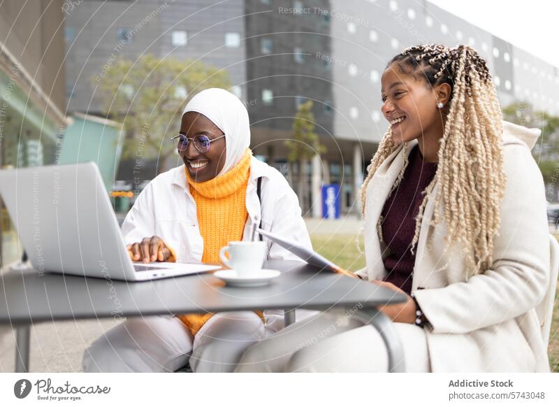 Lächelnde schwarze Frauen mit Laptop in einem Straßencafé Afrikanisch muslimisch Hijab Freundschaft Gerät Apparatur Gespräch im Freien Café Konnektivität