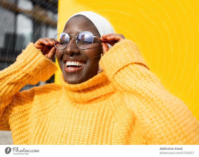Lächelnde Frau in bunter städtischer Umgebung schwarz Afroamerikaner gelb Pullover Brille Mode pulsierend Hintergrund urban Großstadt lässig Straßenkleidung