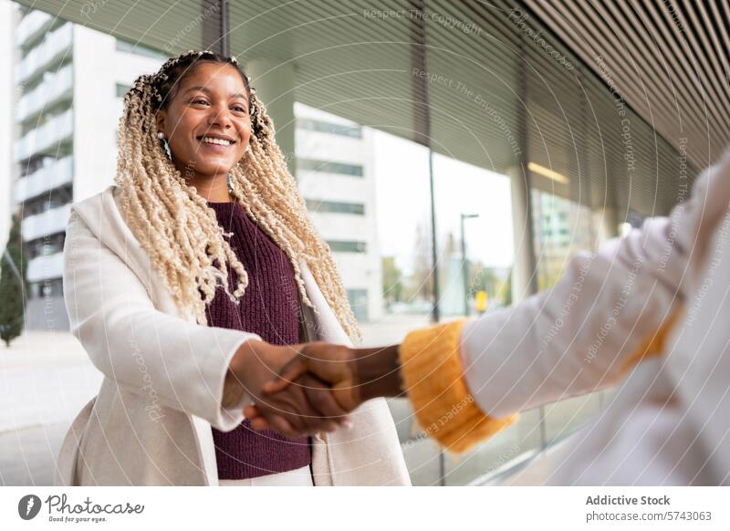 Lächelnde schwarze Frau beim Händeschütteln in der Stadt Afroamerikaner Hände schütteln Großstadt urban im Freien geflochtenes Haar heiter verbindlich Business
